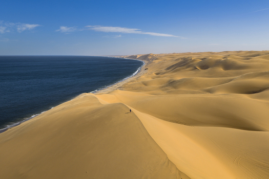 Aerial view of golden dunes meeting the deep blue ocean creating a striking contrast of warm and cool tones Walvis Bay Namibia. Aerial view of golden dunes meeting the deep blue ocean creating a striking contrast of warm and cool tones Walvis Bay Namibia.