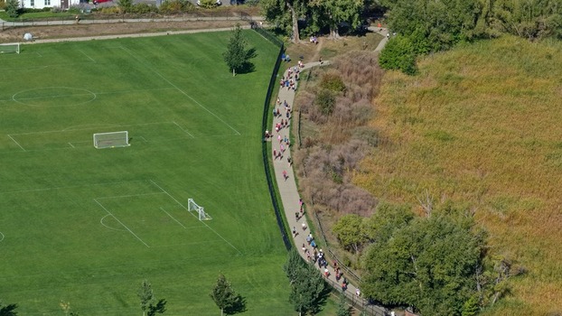 Aerial view of a group of people walking along a paved path next to a green soccer field in a park in Boulder Colorado United States. Aerial view of a group of people walking along a paved path next to a green soccer field in a park in Boulder Colorado United States.