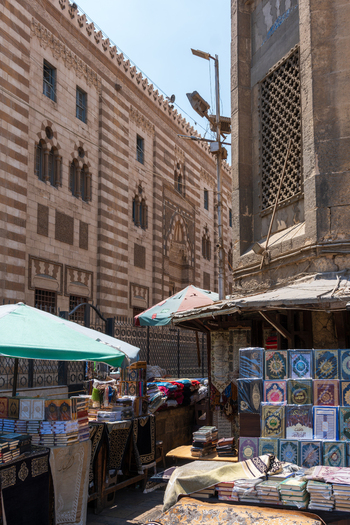 View of Al Azhar Mosque with street market stalls selling books under umbrellas against the historic striped stone walls in Cairo Egypt. View of Al Azhar Mosque with street market stalls selling books under umbrellas against the historic striped stone walls in Cairo Egypt.