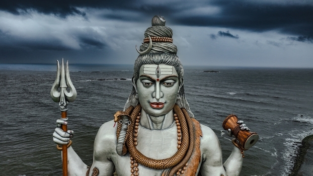 Aerial view of the giant Lord Shiva statue holding a trident and damaru set against the backdrop of the Arabian Sea under a dramatic cloudy sky in Murdeshwar Karnataka India.