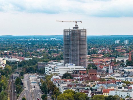 Aerial view of the Steglitzer Kreisel skyscraper covered in scaffolding with a construction crane on top surrounded by the urban landscape of Berlin Berlin Germany. Aerial view of the Steglitzer Kreisel skyscraper covered in scaffolding with a construction crane on top surrounded by the urban landscape of Berlin Berlin Germany.