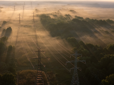 Aerial view of transmission lines and towers rising through dense morning fog over a lush forest landscape at sunrise in Bridgman Michigan United States. Aerial view of transmission lines and towers rising through dense morning fog over a lush forest landscape at sunrise in Bridgman Michigan United States.