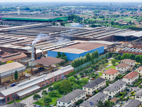 Aerial view of the industrial complex with large warehouses smoking chimneys and residential houses surrounded by green trees in Dalmine Lombardy Italy. Aerial view of the industrial complex with large warehouses smoking chimneys and residential houses surrounded by green trees in Dalmine Lombardy Italy.