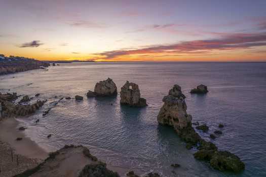 Aerial view of Praia dos Arrifes with its distinctive rock formations and sea stacks rising from the calm ocean waters under a vibrant sunset sky in Faro District Portugal. Aerial view of Praia dos Arrifes with its distinctive rock formations and sea stacks rising from the calm ocean waters under a vibrant sunset sky in Faro District Portugal.