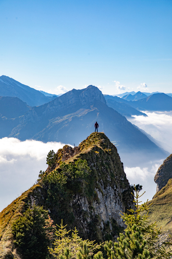 View of a person standing on a rocky peak in the Swiss Alps above a sea of clouds under a clear blue sky in Airolo Ticino Switzerland. View of a person standing on a rocky peak in the Swiss Alps above a sea of clouds under a clear blue sky in Airolo Ticino Switzerland.