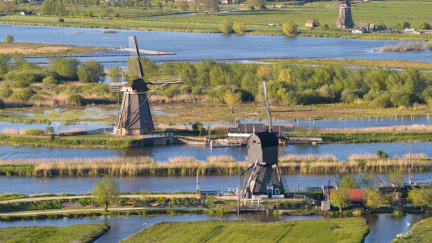 Aerial view of the historic windmills of Kinderdijk standing along the water canals surrounded by lush green polders and reeds under soft sunlight Kinderdijk South Holland Netherlands. Aerial view of the historic windmills of Kinderdijk standing along the water canals surrounded by lush green polders and reeds under soft sunlight Kinderdijk South Holland Netherlands.
