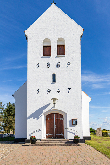 View of Haurvig Kirke featuring its white facade with historic inscriptions wooden entrance door and clear blue sky in Hvide Sande Denmark. View of Haurvig Kirke featuring its white facade with historic inscriptions wooden entrance door and clear blue sky in Hvide Sande Denmark.