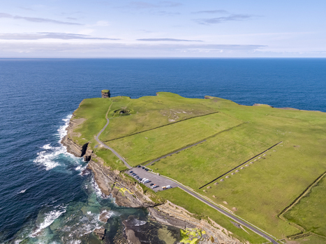 Aerial view of Dun Briste sea stack rising from the Atlantic Ocean surrounded by dramatic green cliffs grassy fields and a coastal parking area in County Mayo Ireland. Aerial view of Dun Briste sea stack rising from the Atlantic Ocean surrounded by dramatic green cliffs grassy fields and a coastal parking area in County Mayo Ireland.