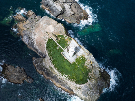 Aerial view of Godrevy Lighthouse on a rocky island surrounded by deep blue sea and crashing waves in Gwithian England United Kingdom. Aerial view of Godrevy Lighthouse on a rocky island surrounded by deep blue sea and crashing waves in Gwithian England United Kingdom.