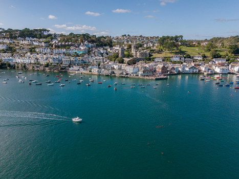 Aerial view of the Fowey river with numerous small boats moored near the historic town featuring stone buildings rooftops and clear blue water in Fowey Cornwall United Kingdom. Aerial view of the Fowey river with numerous small boats moored near the historic town featuring stone buildings rooftops and clear blue water in Fowey Cornwall United Kingdom.
