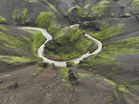 Aerial view of the winding river in the Kerlingarfjoll mountain range featuring moss covered volcanic slopes and dark rocky terrain in Fludir Hrunamannahreppur Iceland. Aerial view of the winding river in the Kerlingarfjoll mountain range featuring moss covered volcanic slopes and dark rocky terrain in Fludir Hrunamannahreppur Iceland.
