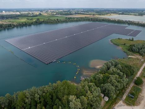 Aerial view of a large floating solar farm installed on a calm lake surrounded by lush green trees and rural landscape in Netherlands. Aerial view of a large floating solar farm installed on a calm lake surrounded by lush green trees and rural landscape in Netherlands.