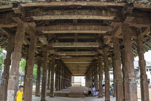Kandy Central Province Sri Lanka 27 April 2026 View of ornate carved wooden pillars inside Sri Dalada Maligawa temple with people resting on the floor and a boy in the foreground. Kandy Central Province Sri Lanka 27 April 2026 View of ornate carved wooden pillars inside Sri Dalada Maligawa temple with people resting on the floor and a boy in the foreground.