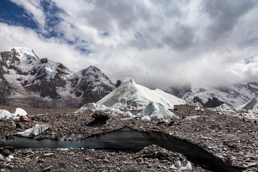 View of Baltoro Glacier with its rugged rocky surface and surrounding snow capped peaks under a cloudy sky in Baltoro Gilgit Baltistan Pakistan.