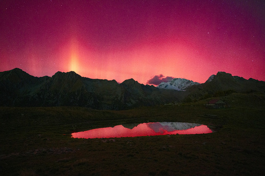 View of the Aurora Borealis glowing red over the Valtellina mountain range with a reflection in a small alpine lake at night in Sondrio Lombardy Italy. View of the Aurora Borealis glowing red over the Valtellina mountain range with a reflection in a small alpine lake at night in Sondrio Lombardy Italy.