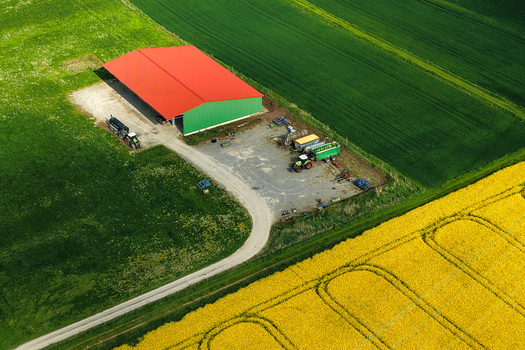 Aerial view of a farm building with a bright red roof surrounded by vibrant green and yellow rapeseed fields Hofgeismar Hessen Germany. Aerial view of a farm building with a bright red roof surrounded by vibrant green and yellow rapeseed fields Hofgeismar Hessen Germany.