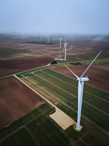 Aerial view of wind turbines piercing the misty horizon standing tall amidst the patchwork fields of green and brown Châteaudun Centre Val de Loire France. Aerial view of wind turbines piercing the misty horizon standing tall amidst the patchwork fields of green and brown Châteaudun Centre Val de Loire France.