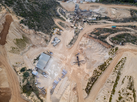 Aerial view of an active quarry site with heavy machinery piles of gravel and industrial processing equipment in Teulada Valencian Community Spain.