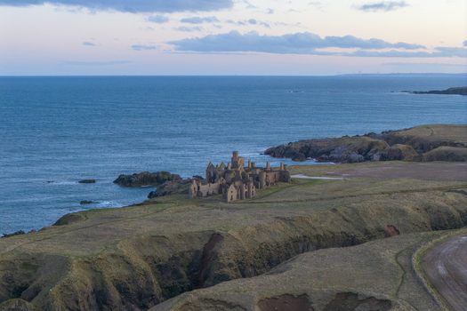 Aerial view of Slains Castle ruins on the rugged cliffs overlooking the North Sea under a soft twilight sky Cruden Bay Scotland United Kingdom. Aerial view of Slains Castle ruins on the rugged cliffs overlooking the North Sea under a soft twilight sky Cruden Bay Scotland United Kingdom.