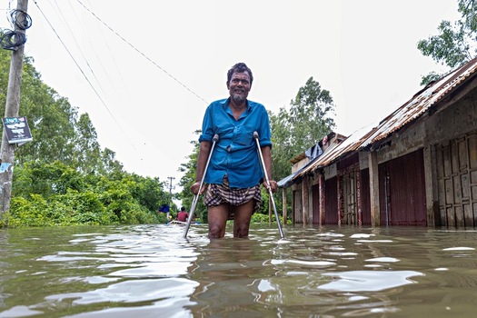 Banshkhali Upazila Bangladesh 10 July 2026 View of a man using crutches standing in floodwater in a rural area with partially submerged buildings. Banshkhali Upazila Bangladesh 10 July 2026 View of a man using crutches standing in floodwater in a rural area with partially submerged buildings.