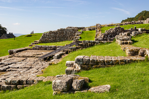 View of the ancient Roman ruins of Vindolanda with stone walls and foundations on grassy slopes under a clear blue sky in Hexham England United Kingdom. View of the ancient Roman ruins of Vindolanda with stone walls and foundations on grassy slopes under a clear blue sky in Hexham England United Kingdom.