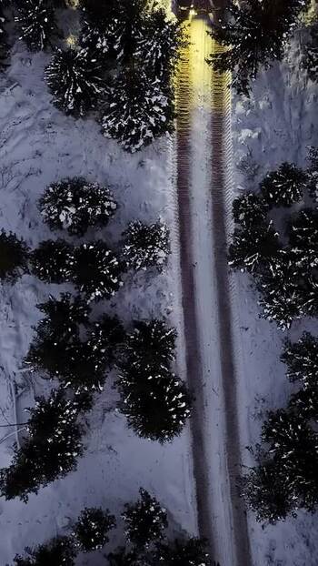 Aerial view of snowy road through forest in Latvia.