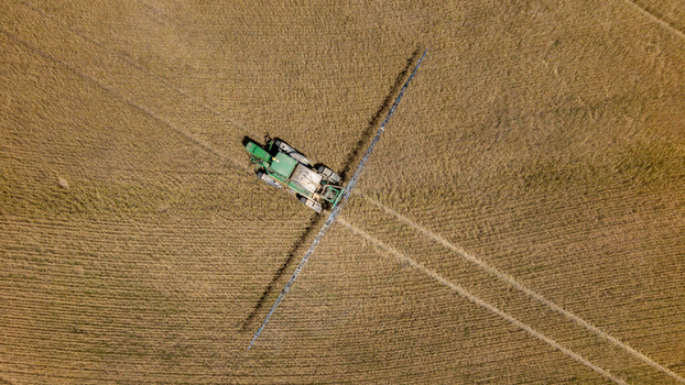 Aerial view of a green tractor with a long spray boom working in a golden agricultural field with visible tire tracks in Philadelphia Western Cape South Africa. Aerial view of a green tractor with a long spray boom working in a golden agricultural field with visible tire tracks in Philadelphia Western Cape South Africa.