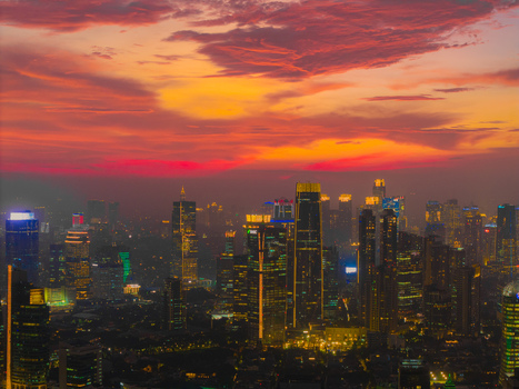 Aerial view of the Jakarta skyline at sunset with illuminated skyscrapers and vibrant orange clouds over the city Tebet Jakarta Indonesia.