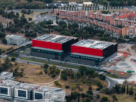 Aerial view of modern datacenter facility with distinctive red and black exterior walls surrounded by roads trees and urban infrastructure in Settecamini Lazio Italy.