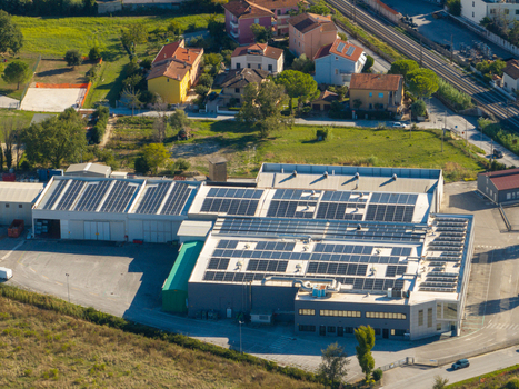 Aerial view of an industrial facility featuring extensive solar panel arrays on its roof surrounded by green fields residential houses and nearby railway tracks in Ancona Marche Italy. Aerial view of an industrial facility featuring extensive solar panel arrays on its roof surrounded by green fields residential houses and nearby railway tracks in Ancona Marche Italy.