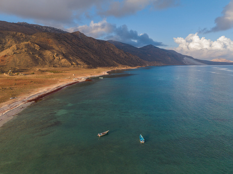 Aerial view of the coastline meeting the turquoise waters with boats gently bobbing framed by rugged mountains under a sky Dhi Hamri Socotra Yemen. Aerial view of the coastline meeting the turquoise waters with boats gently bobbing framed by rugged mountains under a sky Dhi Hamri Socotra Yemen.