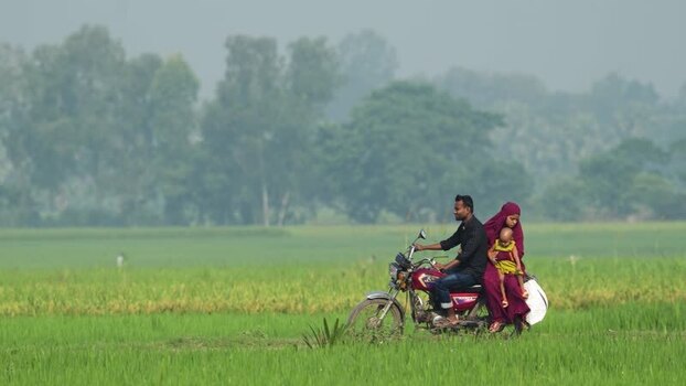 View of a family on a motorcycle in a green field Bangladesh.