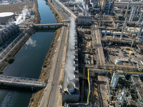 Aerial view of an industrial refinery complex with cooling towers emitting steam complex pipe networks and a canal in Carson California United States.