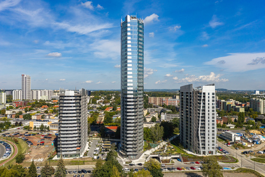 Aerial view of modern residential real estate featuring a prominent glass skyscraper surrounded by contemporary apartment buildings and green spaces in Katowice Silesian Voivodeship Poland.