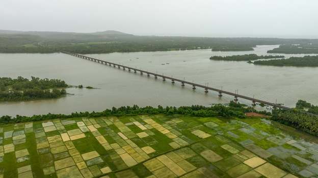 Aerial view of the railway bridge spanning the Sharavathi River surrounded by lush green paddy fields and rural landscape in Honnavar Karnataka India.
