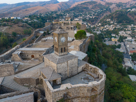 Aerial view of Gjirokaster Fortress with its prominent clock tower stone walls and historic architecture overlooking the town of Gjirokaster Gjirokaster County Albania. Aerial view of Gjirokaster Fortress with its prominent clock tower stone walls and historic architecture overlooking the town of Gjirokaster Gjirokaster County Albania.
