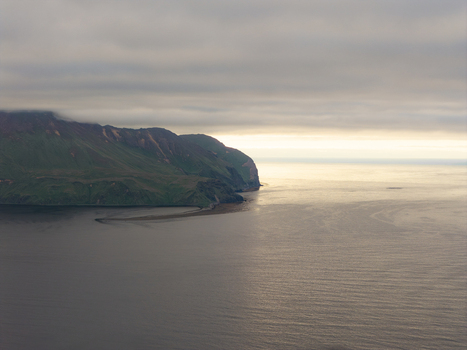 Aerial view of the rugged coastline and green hills of Unalaska under a cloudy sky at sunset in Unalaska Alaska United States.