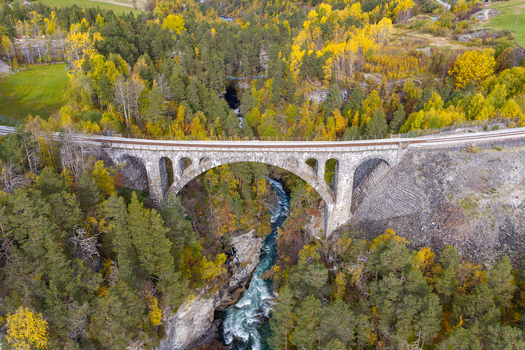 Aerial view of the historic stone arch Kylling Bridge spanning the Rauma River surrounded by vibrant autumn forest and rocky terrain in Verma More og Romsdal Norway. Aerial view of the historic stone arch Kylling Bridge spanning the Rauma River surrounded by vibrant autumn forest and rocky terrain in Verma More og Romsdal Norway.