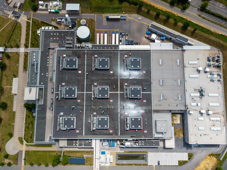 Aerial view of a large industrial warehouse with flat roofs ventilation units and loading docks surrounded by parking and green spaces in Zebrak Central Bohemian Region Czechia. Aerial view of a large industrial warehouse with flat roofs ventilation units and loading docks surrounded by parking and green spaces in Zebrak Central Bohemian Region Czechia.