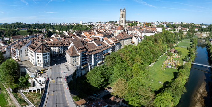 Aerial view of St Nicolas Cathedral and the historic old town with medieval architecture red rooftops and the Sarine river surrounded by lush green forests in Fribourg Fribourg Switzerland. Aerial view of St Nicolas Cathedral and the historic old town with medieval architecture red rooftops and the Sarine river surrounded by lush green forests in Fribourg Fribourg Switzerland.