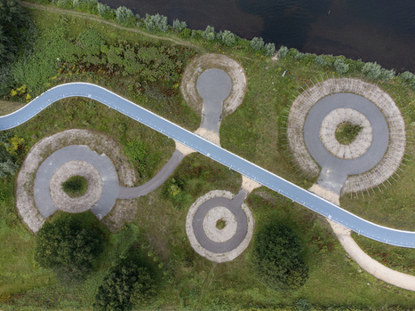 Aerial view of a winding blue path connecting circular platforms amidst green fields and a dark river s edge Utopia Flevoland Netherlands.