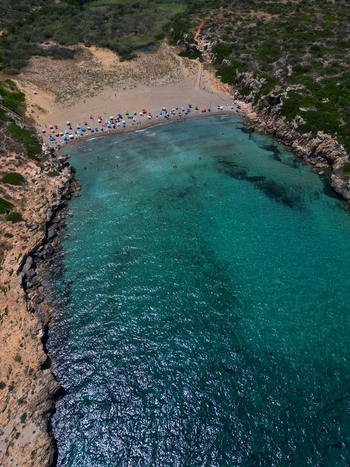Aerial view of Calamosche Beach with turquoise water rocky cliffs and people on the sand in Noto Sicilia Italy.