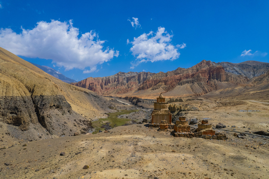 Aerial view of ancient stone stupas situated in a rugged arid mountain landscape with dramatic rock formations under a clear blue sky in Nepal.