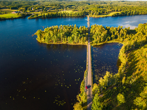 Aerial view of a road crossing a lake surrounded by lush green forests and trees in the golden hour light in Gallared Halland County Sweden. Aerial view of a road crossing a lake surrounded by lush green forests and trees in the golden hour light in Gallared Halland County Sweden.