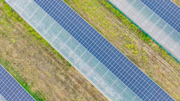 Aerial view of photovoltaic solar panels installed on modern agricultural greenhouses surrounded by grassy fields Loriol sur Drome Auvergne Rhone Alpes France.