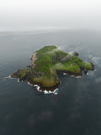 Aerial view of a small green island surrounded by dark ocean waters and mist in Iceland. Aerial view of a small green island surrounded by dark ocean waters and mist in Iceland.