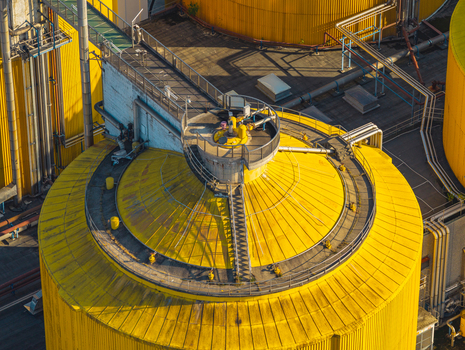 Aerial view of a large yellow industrial storage tank at a wastewater treatment and environmental infrastructure complex in Italy.