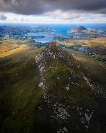 Aerial view of Diamond Hill peak overlooking the rugged landscape and coastal lakes under a dramatic cloudy sky in County Galway Ireland. Aerial view of Diamond Hill peak overlooking the rugged landscape and coastal lakes under a dramatic cloudy sky in County Galway Ireland.