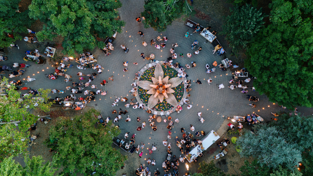 Aerial view of people gathering around a large flower shaped fountain in a park with string lights and lush trees in Sremska Mitrovica Serbia. Aerial view of people gathering around a large flower shaped fountain in a park with string lights and lush trees in Sremska Mitrovica Serbia.