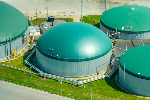 Aerial view of a biogas plant featuring large green domed storage tanks for fermented mass connected by industrial metal piping situated in Poland.